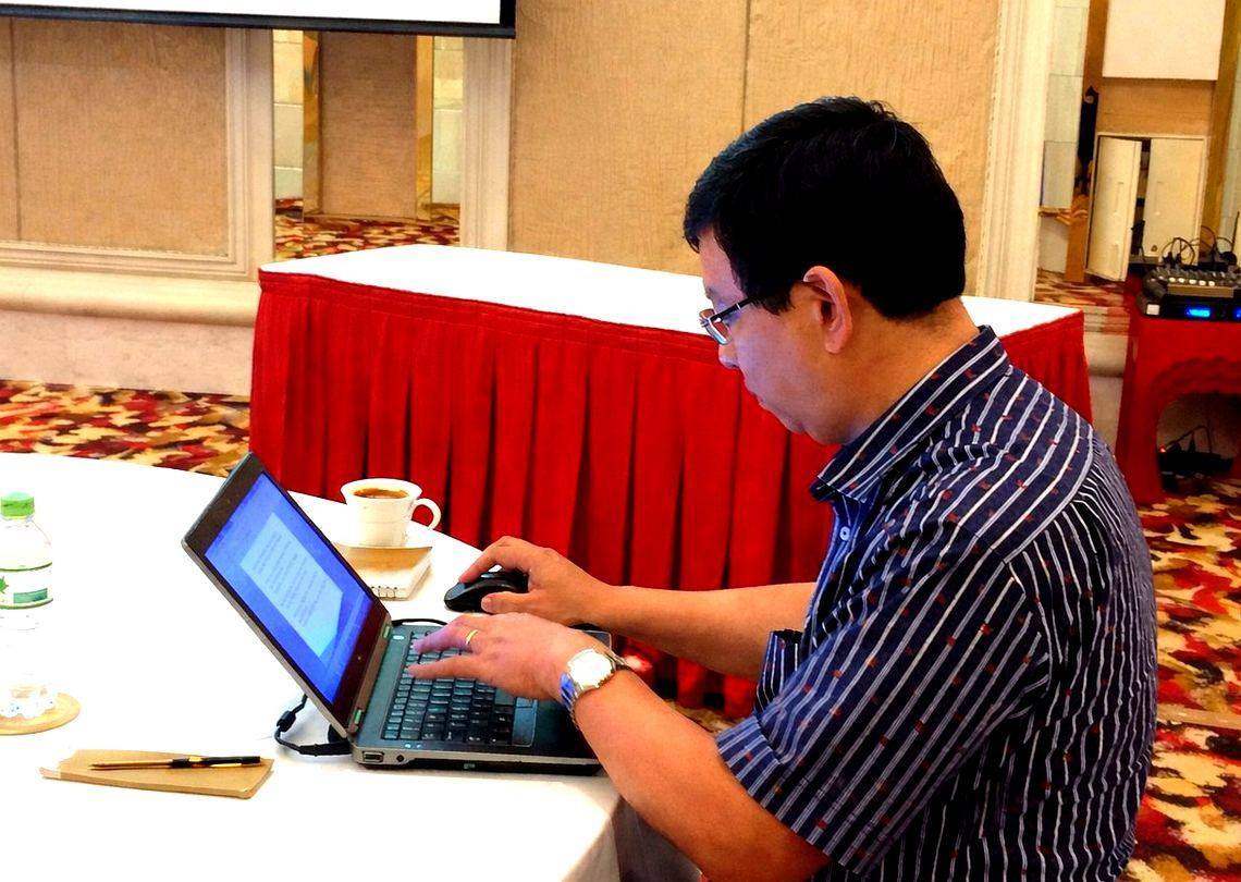 Dr. Phuong Nguyen working on a laptop at a hotel function room, between conference sessions